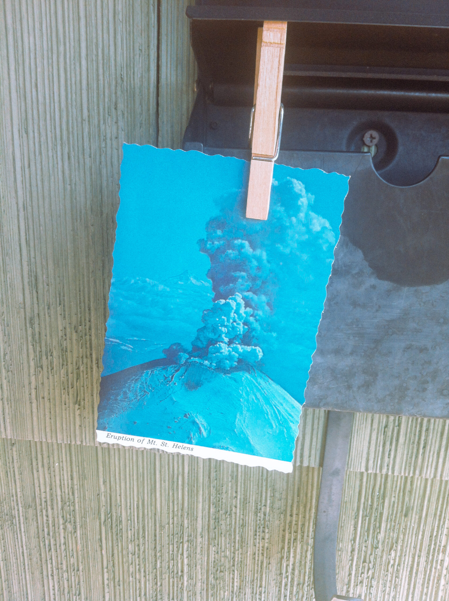 A postcard of Mount St. Helens erupting held with a clothespin to a mailbox